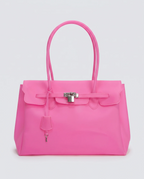 A bright pink jelly handbag with silver-tone hardware, featuring a front flap, top handles, and a hanging clochette, photographed against a light gray studio background.
