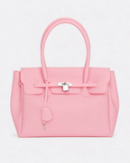 A baby pink jelly handbag with silver-tone hardware, featuring a front flap, top handles, and a hanging clochette, photographed against a light gray studio background.