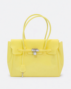 A bright yellow structured handbag with double top handles, a front flap, a drawstring detail, and a silver padlock closure, photographed against a clean white background.